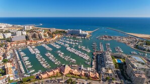 An aerial view of a marina with numerous boats docked, surrounded by buildings and a clear view of the sea. - Vilamoura Center - Near Marina By Vilamoura Sun (Quarteira)