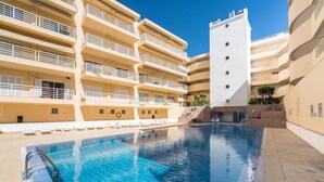 A swimming pool with a clear blue water surface, surrounded by a multi-story building with balconies and a white tower. - Vilamoura Center - Near Marina By Vilamoura Sun (Quarteira)