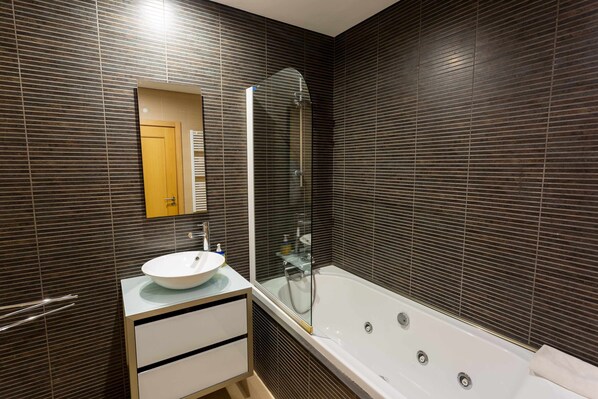 A modern bathroom with a large bathtub, a glass-enclosed shower, and a white vanity with a sink. - VilamouraSun Aquamar 513 - Overlooking garden (Quarteira)