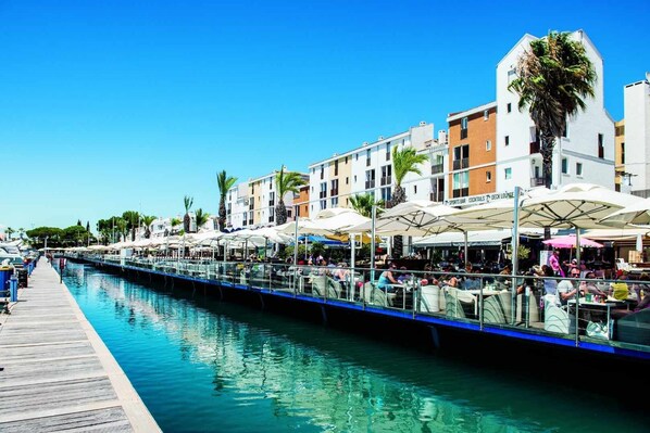 A canal-side bar with outdoor seating, a pool, and buildings with balconies.
