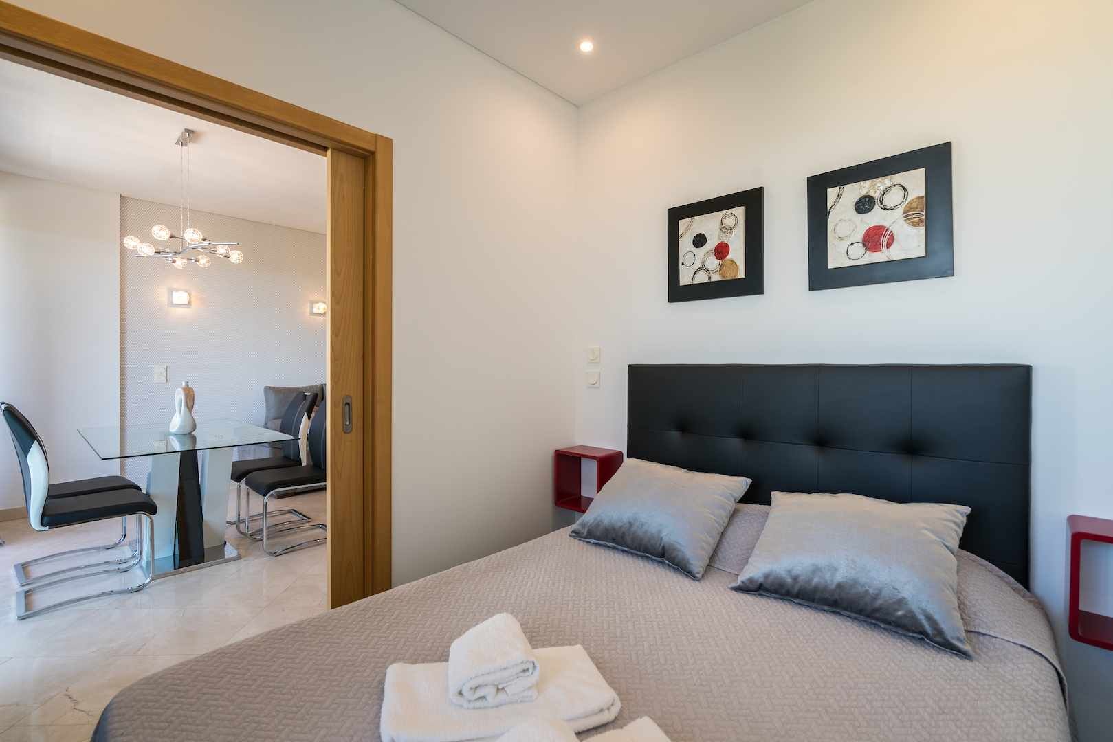 A modern hotel room with a large bed, two bedside tables, a desk with chairs, and artwork on the wall.