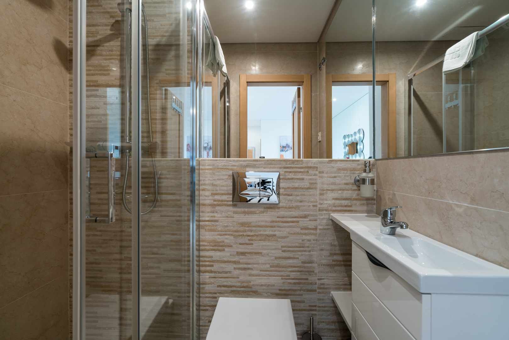 A modern bathroom with a glass-enclosed shower, a white sink, and a mirror.