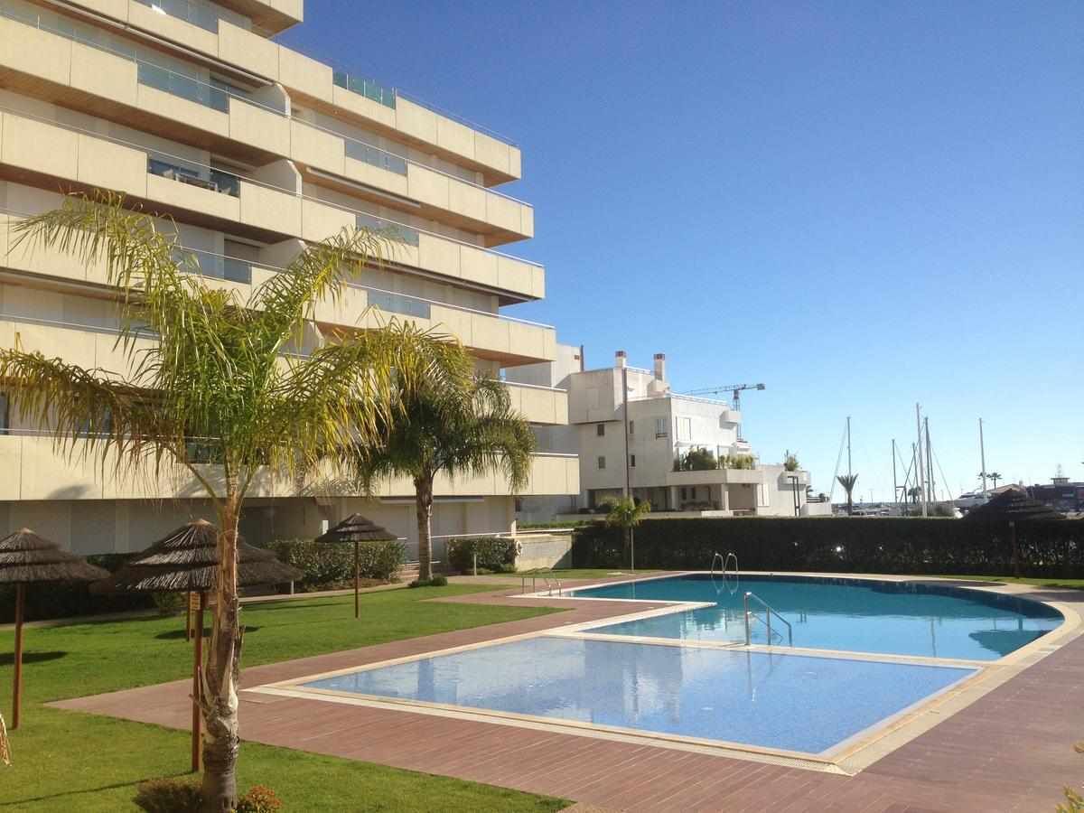 A modern building with a swimming pool, palm trees, and a clear sky.