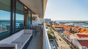 Un balcon avec un canapé et des fauteuils, donnant sur une marina et des immeubles.
