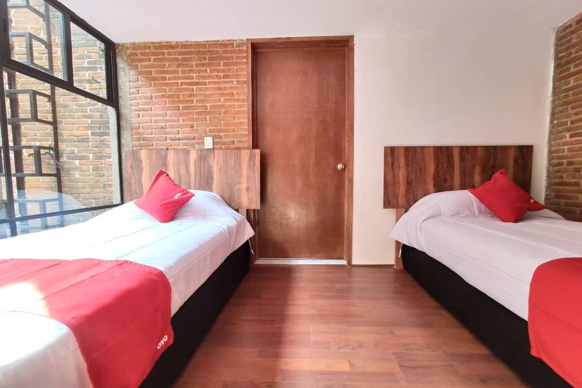A hotel room with two beds, a wooden headboard, a brick wall, and a large window.