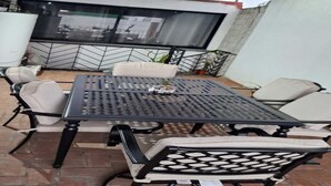 Un patio al aire libre con una mesa de metal negro y sillas con cojines color beige.