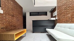 Un interior moderno con pared de ladrillo, un sofá blanco, un banco de madera y un cabecero negro.