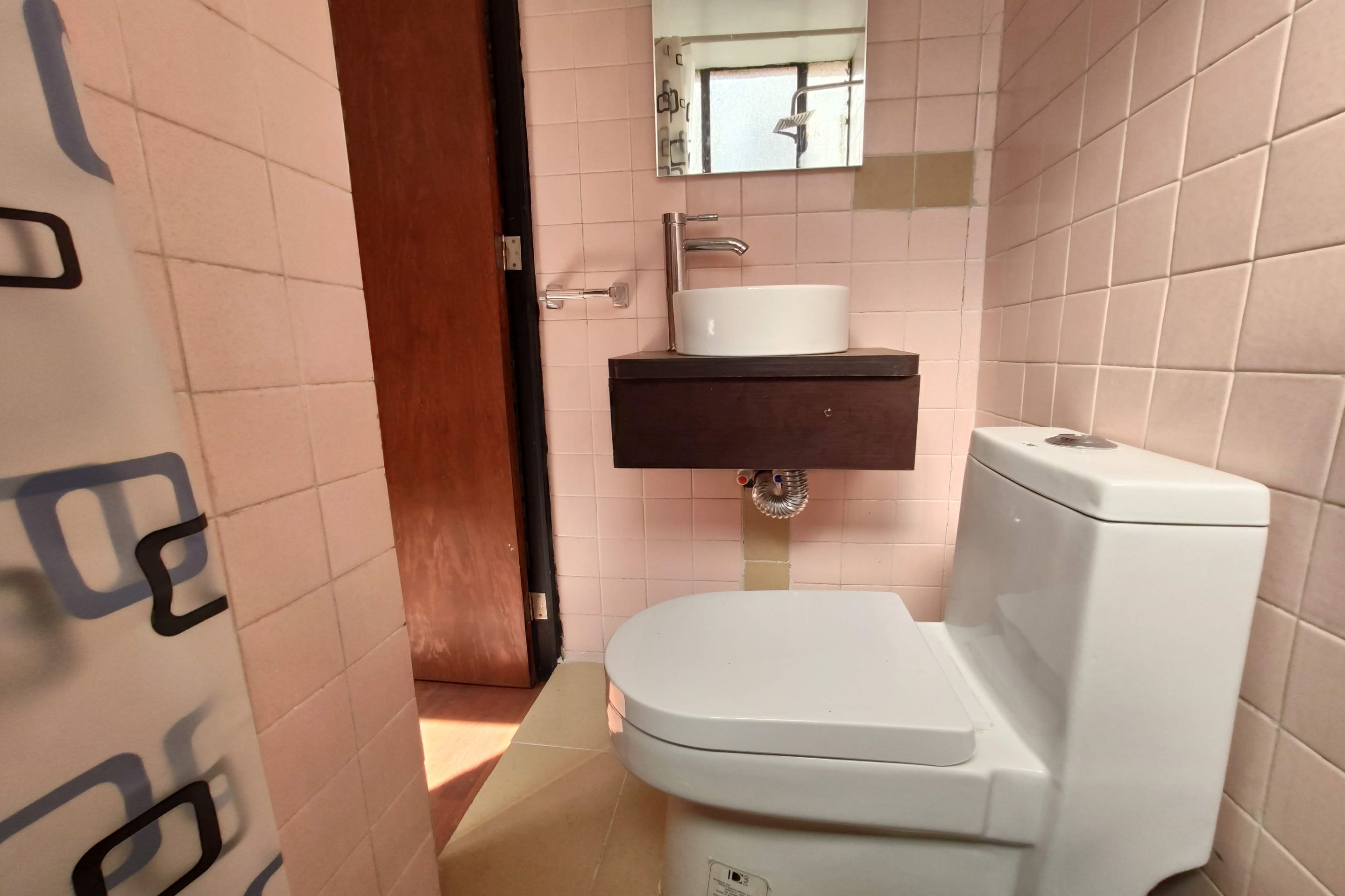 A bathroom with a white toilet, a sink with a mirror above it, and a door leading to another room.