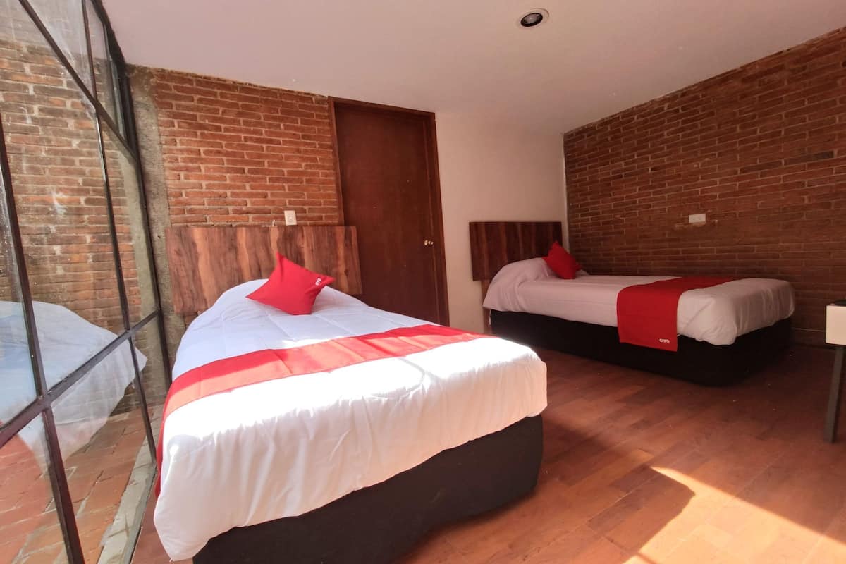 A hotel room with two beds, a brick wall, and a large window.