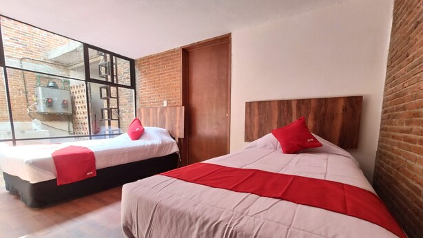 Dos camas con almohadas rojas, un cabecero de madera y una pared de ladrillo.