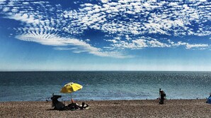 A beach with a pebbled shore, a yellow umbrella, and a person relaxing under it. - Georgian Seafront fisherman’s cottage | Sea views | Old Town (Hastings)