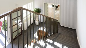 Una escalera con barandilla de madera, una planta en maceta y vista a un comedor con mesa y sillas.
