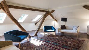 Habitación estilo loft con vigas de madera a la vista, un sillón azul, un sofá color beige y una alfombra estampada.