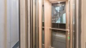 An elevator with metallic walls and a glass panel, featuring a metallic handrail and a green emergency button. - Apartment Paris Center "Marais" - 4 people (Paris)