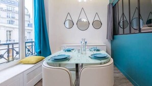 A dining area with a table set for four, a window with a view of buildings, and a blue curtain. - Apartment Paris Center "Marais" - 4 people (Paris)