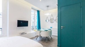 A modern hotel room with a large bed, a dining area with a table and chairs, a TV mounted on the wall, and a teal door. - Apartment Paris Center "Marais" - 4 people (Paris)