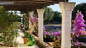 A covered walkway with stone columns, potted plants, and flowering plants. - Masseria Sottomasi (Fasano)
