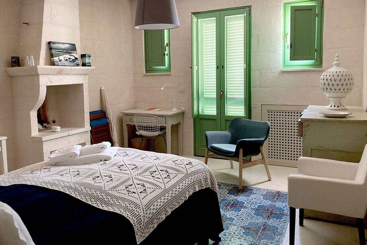 A bedroom with a bed, a desk, a chair, a radiator, and a window with shutters.