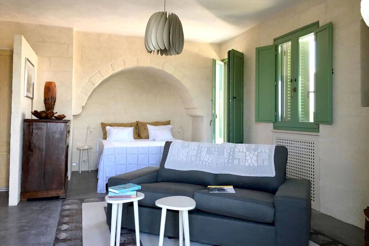 A cozy room with a bed, a sofa, two small tables, and a decorative cabinet.