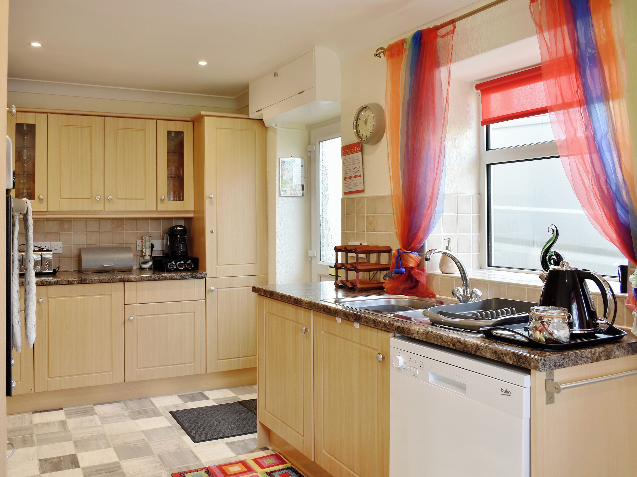 A kitchen with wooden cabinets, a coffee maker, a kettle, and a sink.