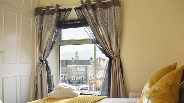 Une chambre à coucher avec un lit, une fenêtre avec des rideaux et une vue sur les bâtiments à l’extérieur.