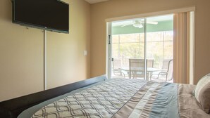 A bedroom with a bed, a TV mounted on the wall, and a sliding glass door leading to an outdoor area with chairs. - 3 Bed 258 (Kissimmee)