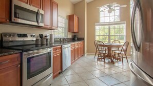 A kitchen with wooden cabinets, stainless steel appliances, and a dining area with a table and chairs. - 3 Bed 258 (Kissimmee)