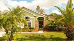 A two-story house with a green and beige exterior, a brick entrance, and a well-maintained lawn with palm trees. - 3 Bed 258 (Kissimmee)