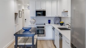 A modern kitchen with white cabinets, a stainless steel refrigerator, a double oven, and a sink. - Remodeled Beachfront Mission Beach Condo on the boardwalk with Amazing Views! (San Diego)