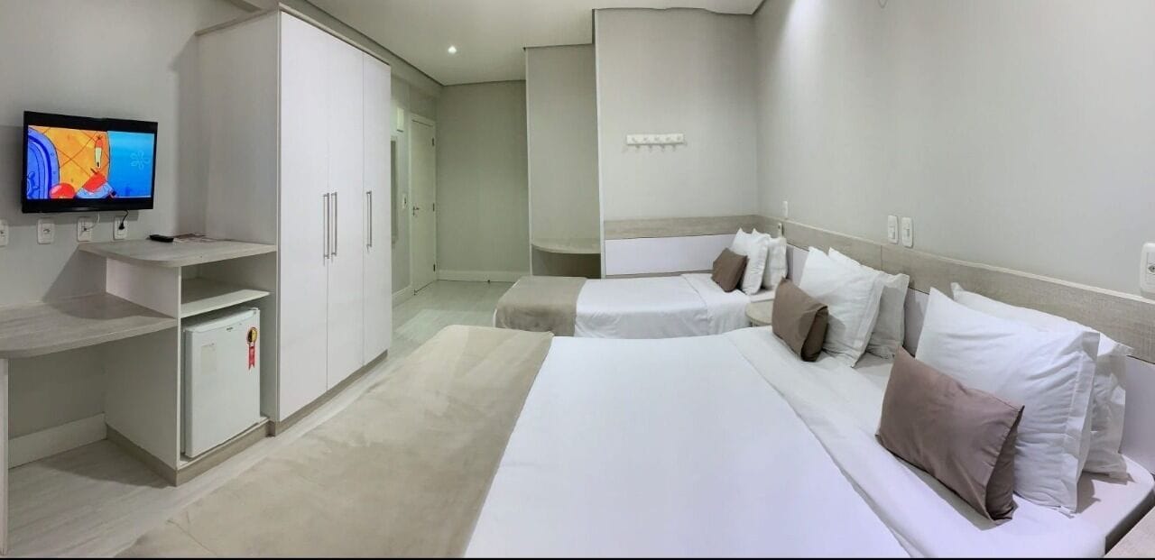A hotel room with a large bed, a TV, a wardrobe, and a small fridge.