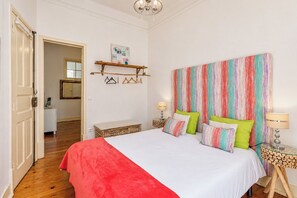 A bedroom with a bed, bedside tables, a mirror, and a door leading to another room.