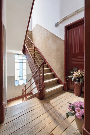 A wooden staircase with a handrail, a potted plant, and a door with a window above it.
