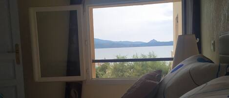A bedroom with a bed, a window, and a view of a lake and mountains.