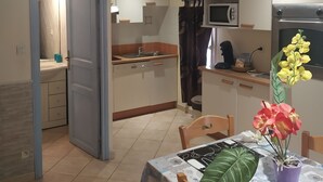 A compact kitchen with a microwave, oven, and sink. There is a dining area with a table and chairs, and a potted plant on the table. - F2 apartments with panoramic sea views (corse)