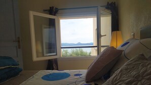 A bedroom with a bed, a window with a view of mountains, and a lamp. - F2 apartments with panoramic sea views (corse)