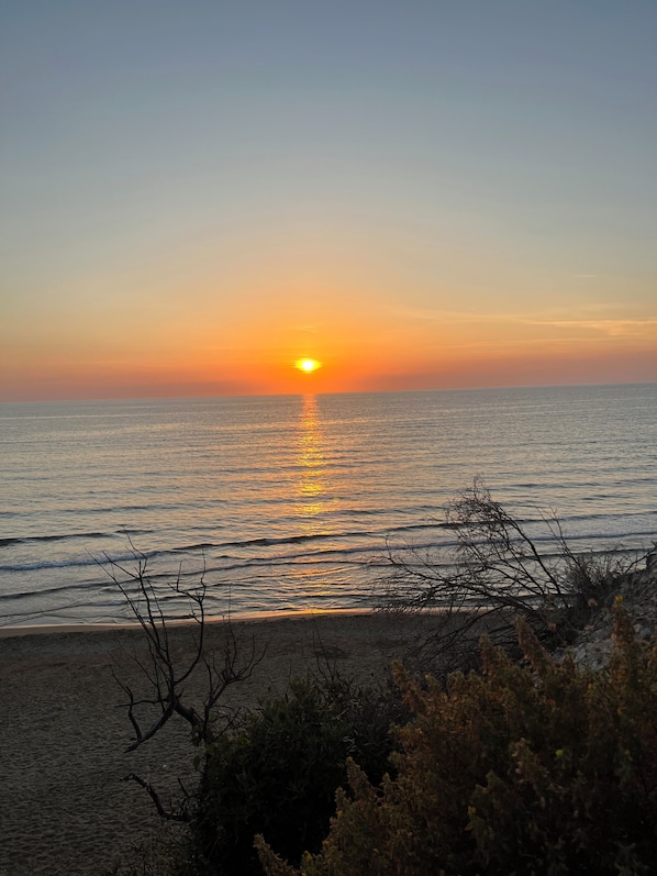 Un atardecer sobre un mar tranquilo con una playa en primer plano.
