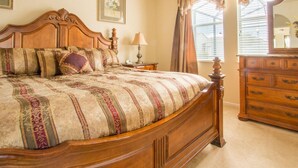 A bedroom with a large wooden bed, a nightstand, a dresser, and a window with curtains.