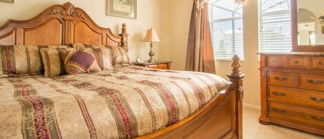 A bedroom with a large wooden bed, a nightstand, a dresser, and a window with curtains.