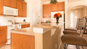A kitchen with wooden cabinets, a white microwave, a granite countertop, and a small island with bar stools.