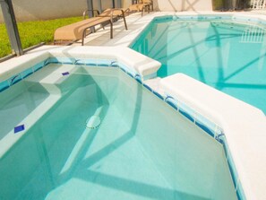 A swimming pool with a clear blue water feature, surrounded by lounge chairs and a grassy area.