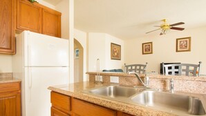 A kitchen with wooden cabinets, a white refrigerator, granite countertops, a double sink, and a ceiling fan.