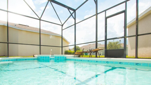 An indoor swimming pool with clear blue water, surrounded by a glass enclosure with a metal frame.