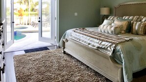 Een slaapkamer met een bed, uitzicht op een zwembad en een deur naar buiten.