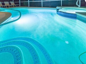 A swimming pool with a curved design, a hot tub, and lounge chairs.