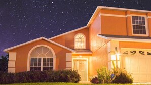 Een twee verdiepingen tellend huis met garage, rondboogvensters en een helder verlichte voordeur.