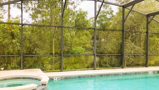 Une piscine dotée d’une structure en verre, entourée d’arbres.