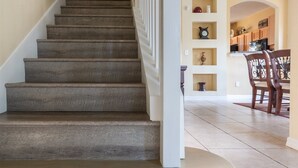 Un escalier avec une rampe, menant à une cuisine équipée de meubles en bois et comprenant une table à manger.