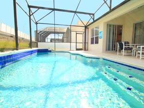 Ein Hallenbad mit klarem, blauem Wasser, umgeben von einer Glasfassade und einer Terrasse mit Sitzgelegenheiten.
