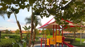 A playground with a red and yellow play structure, surrounded by lush greenery and a clear sky. - Private Screened Splash Pool Overlooking Tranquil Lake Right Beside Disney World by Florida Dream Homes (Kissimmee)