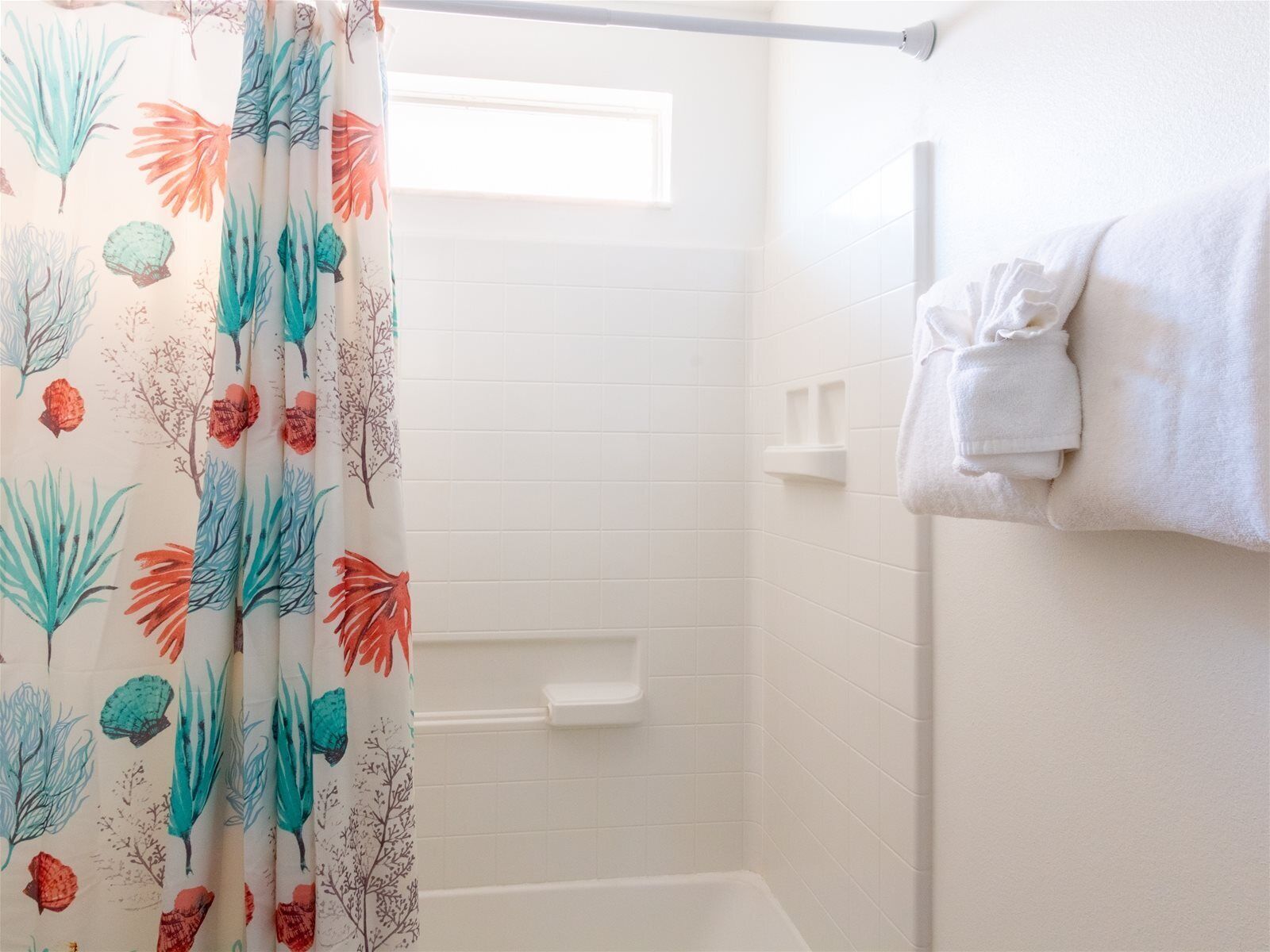 A bathroom with a shower curtain featuring a tropical leaf pattern, white tiled walls, and a towel rack with folded towels.